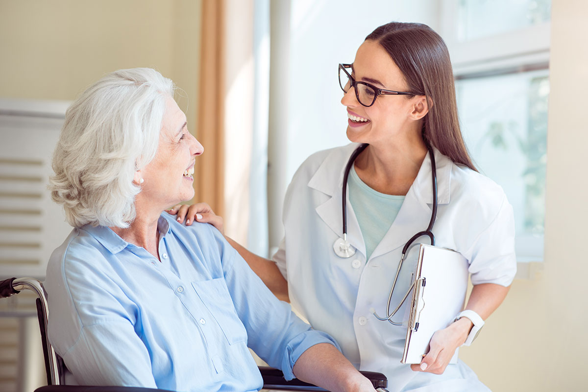 Nice, friendly nurse talking to senior female patient seated in a wheelchair.