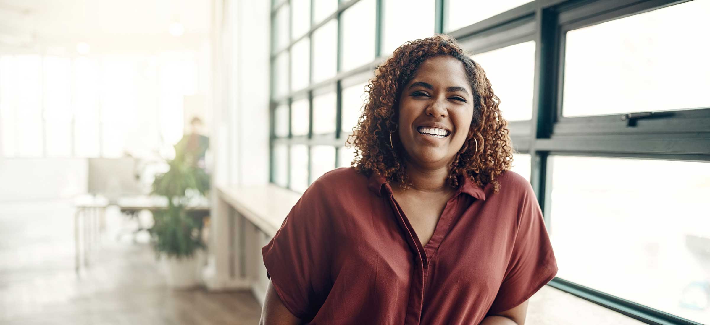 A woman with curly hair smiles by a window.
