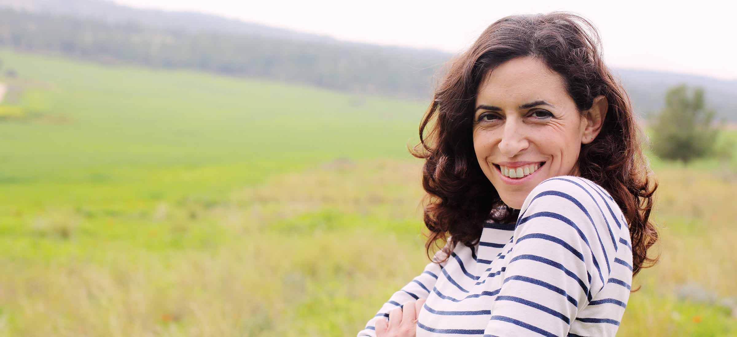 40-year-old brunette woman smiles outdoors.