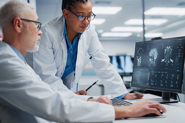 Happy neurologist and neurosurgeon talk in front of a computer with a brain scan on the screen.