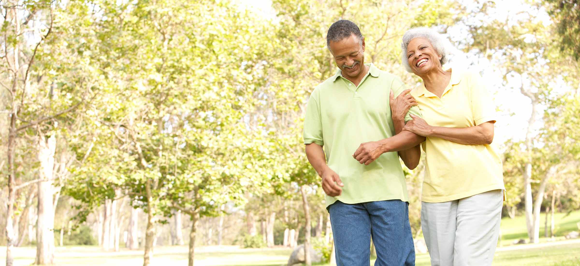 A man and woman walk in a park while holding arms together.