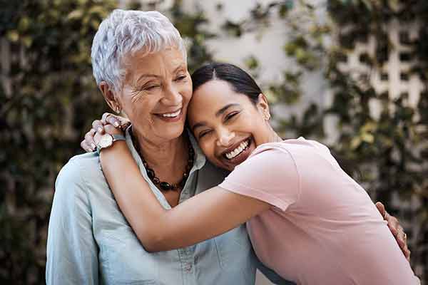A mother and her adult daughter hug and smile in a garden