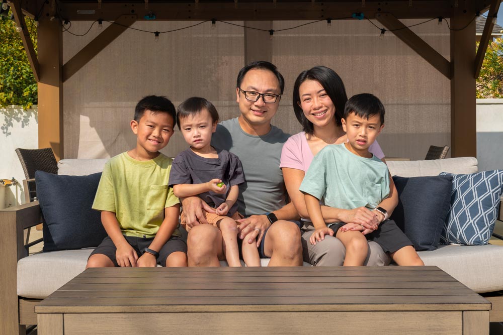 Annie Cheung sits with her husband and three sons outside on a silver couch