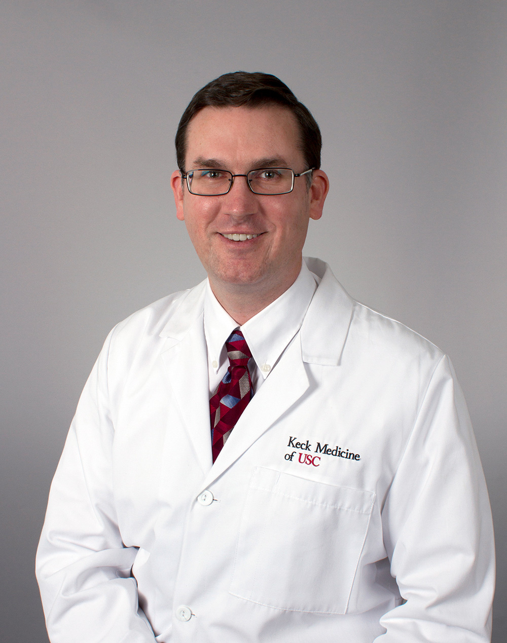 Dr. Cologne stands in a white medical coat against a grey background