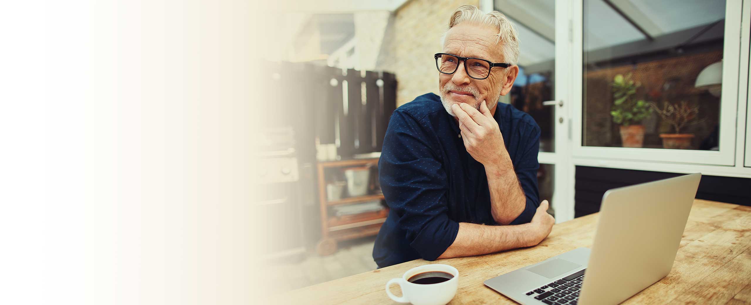 A man smiles while sitting at a table in front of a laptop.