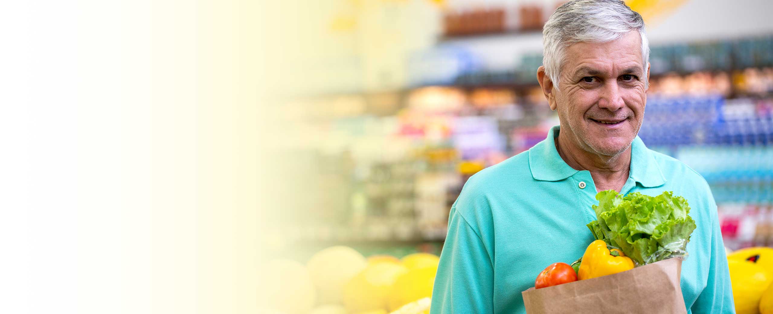 A man holds a bag of groceries and smiles.