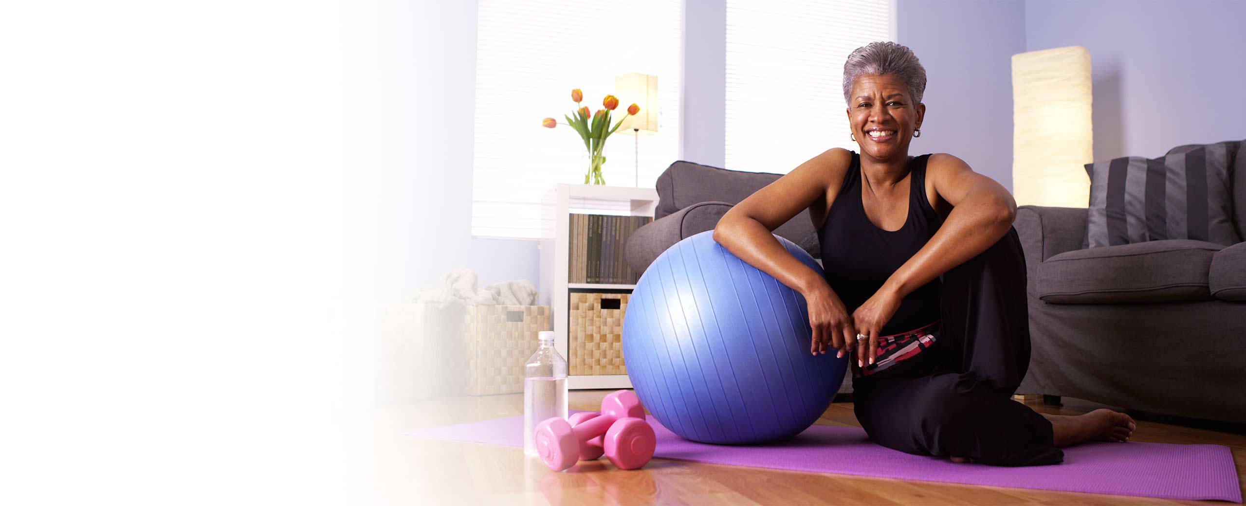 A woman sits on the ground with an exercise ball.