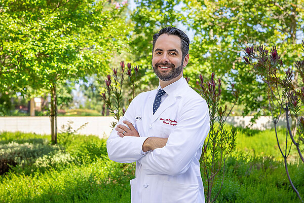Dr. Rosenberg stands in a white medical coat in front out some trees, smiling